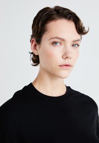 Melna, ar apaļu kakla izgriezumu, T-kreklu, kas izgatavots no gludas auduma, cieši pieguļošs dizains ar īsām piedurknēm, ar minimālu šuvju skaitu un mīkstu tekstūru.