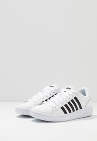 White athletic shoes with six black stripes on the sides, a rubber sole, and cushioned tongue and collar for comfort.