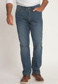 Jeans in denim blu scuro con design a gamba dritta, cinque tasche, leggero effetto consumato e cuciture a contrasto, abbinati a stivali marroni con lacci.