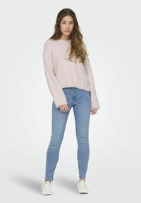 Pull en rose pâle, texturé, avec des manches larges, associé à un jean bleu taille haute et ajusté, ainsi qu'à des baskets blanches. Tenue simple et décontractée.