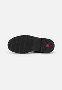 Black rubber shoe sole with textured pattern, featuring horizontal grooves and embossed brand logo. Red circular detail near heel.