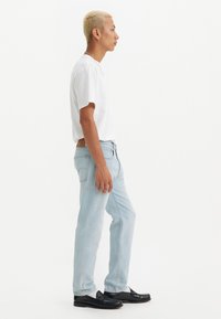 Jeans de mezclilla azul claro con un diseño de corte recto, combinados con una camiseta blanca de manga corta y mocasines negros. Textura lisa, sin patrones.