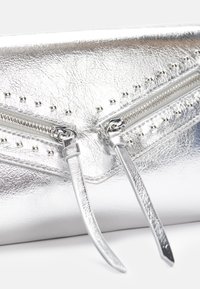 Hopea metallinen laukku, jossa on kaksi vetoketjua, niittikoristeita ja sileä pinta. Varustettu pitkillä hihnoilla turvallista sulkemista varten.