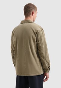 Khaki corduroy overhemd met lange mouwen, een kraag en knoopmanschetten; heeft verticale ribbels en een ontspannen pasvorm.