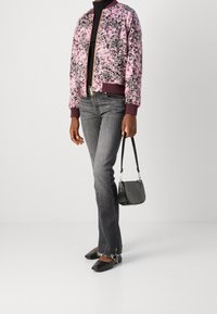 Bloemmotief bomberjack in roze en zwart met geribde manchetten, gecombineerd met grijze spijkerbroek, zwarte flats en een kleine zwarte handtas.