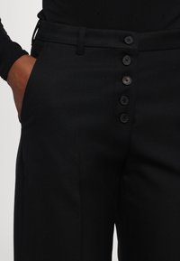 Svarta skräddarsydda byxor i texturerad tyg med hög midja och en rad med sex svarta knappar i fronten.