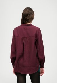 Μαρο�ύλι μακρυμάνικο πουκάμισο από ελαφρύ ύφασμα, με πτυχές στην πλάτη, κουμπιά στους καρπούς και διακριτική κεντημένη λεπτομέρεια στον γιακά.