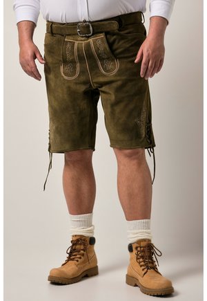 Mand iført brune læder traditionelle bayerske shorts med broderi, hvide sokker, tan snørebåndsstøvler og en hvid langærmet skjorte.