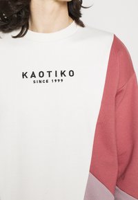 Felpa leggera con collo a giro, caratterizzata da un corpo bianco e maniche color block in rosa e lilla. Logo ricamato nero sul petto.
