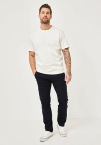 Weißes Baumwoll-T-Shirt mit kurzen Ärmeln, kombiniert mit navyfarbenen Twill-Hosen und weißen Sneakern, präsentiert einen lässigen Schnitt und ein minimales Design.