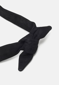 Ceinture en daim noir avec un design noué, présentant deux extrémités allongées qui se terminent en pointes. Texture douce avec une finition mate.