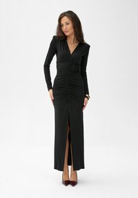 Černé dlouhé šaty s hlubokým výstřihem do V, nařízeným předním dílem a bočním rozparkem; vyrobené z jemného materiálu s obtáhlým střihem.