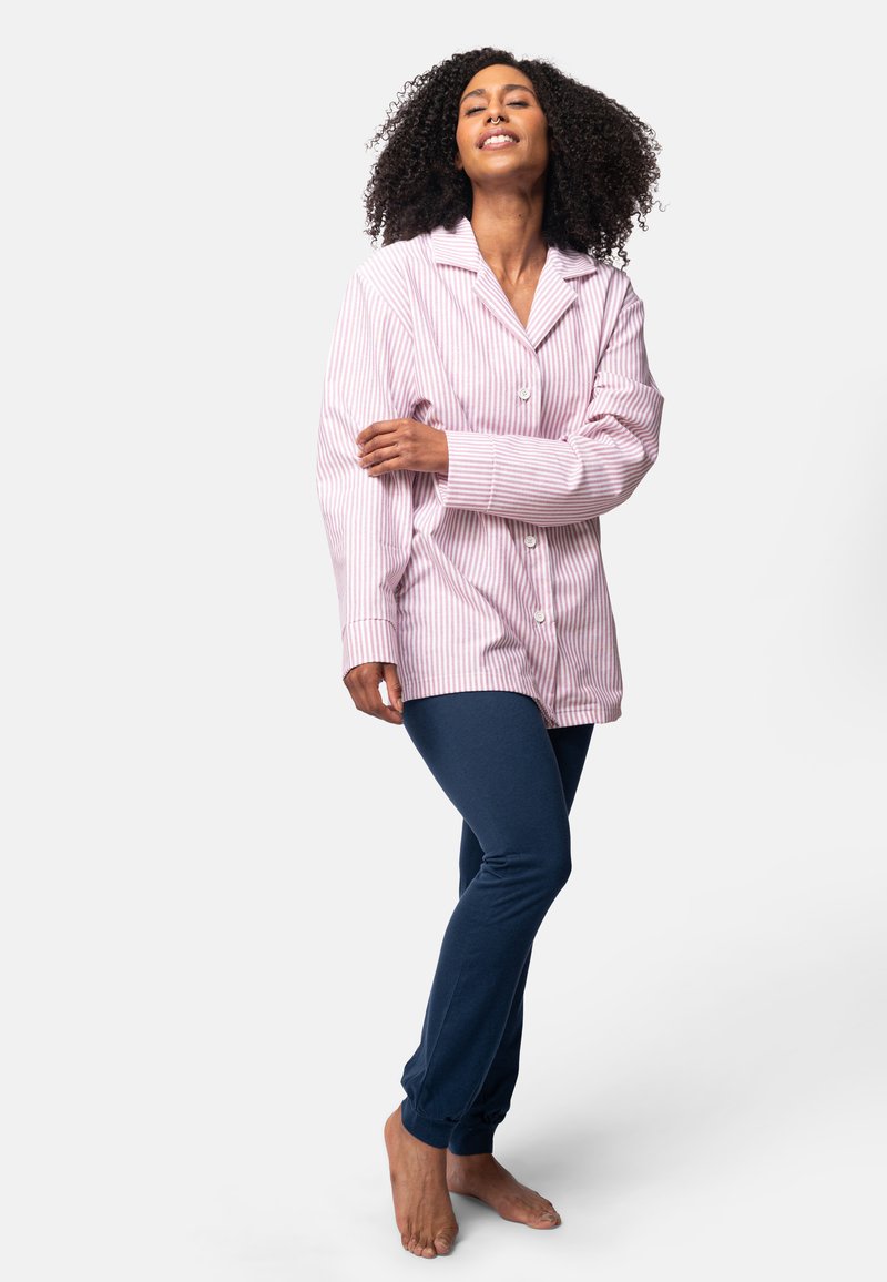 Camicia da pigiama a righe rosa e bianche con bottoni e maniche lunghe, abbinata a pantaloni fitted blu navy, indossati a piedi nudi.