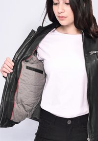 Svart läderjacka med ett vadderat grått foder, prydd med röda detaljer och en dragkedjeficka. Modellen håller jackan öppen och visar foderet.