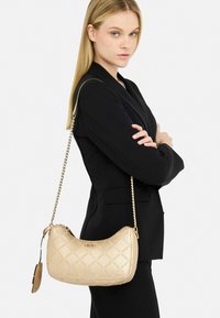 Borsa a spalla in similpelle dorata con forma curvilinea, design trapuntato, tracolla a catena e dettagli con marchio. Presenta una texture liscia.