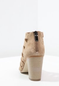 Beige mokkasini-ankkuri saappaat avoimilla sivuilla, takana vetoketju ja teksturoitu pinottu korko. Varustettu sileällä pohjalla ja minimalistisella muotoilulla.