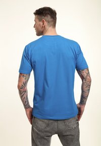 Modré bavlněné tričko s krátkými rukávy, kulatým výstřihem a hladkou strukturou. Zadní pohled ukazuje jednoduchý design bez viditelných log nebo vzorů.