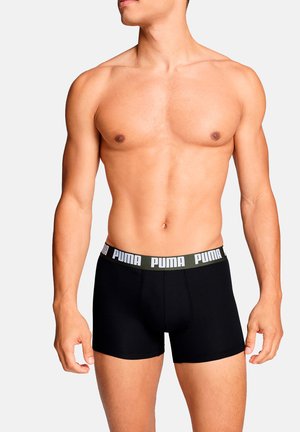 Schwarze Boxershorts mit einem breiten grünen und weißen Markenbund, die ein eng anliegendes Design und eine glatte Textur aufweisen. Modell seitlich gezeigt.