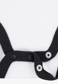 Hvit stoff overall med svart kontrastbind og trykknapper. Glatt tekstur, med runde trykknapper for enkel bruk.