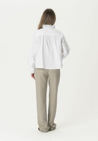White, long-sleeve blouse with ruffled collar detail, paired with beige, loose-fitting trousers. The design features a gathered back.