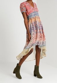 Robe à motifs multicolores avec des manches courtes bouffantes, un décolleté en V profond et un ourlet asymétrique. Associée à des bottes chevilles vert olive.