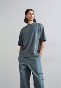 Camiseta gris de gran tamaño hecha de un material suave, con un estampado azul. Combinada con pantalones cargo gris claros con bolsillos con cremallera y detalles.