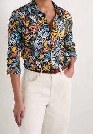Bloemen blouse met knopen met een marineblauwe achtergrond en meerkleurige bloemenpatronen. Gecombineerd met off-white broek en een gevlochten bruin leren riem.