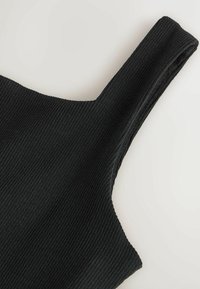 Gros plan sur un débardeur en tissu côtelé noir montrant la sangle texturée et l'encolure sur un fond clair.