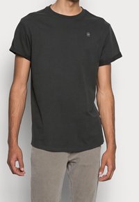 Czarna koszulka z krótkim rękawem wykonana z bawełny. Okrągły dekolt z subtelnym logo na piersi. Luźny fason, gładka tekstura, nowoczesny design.