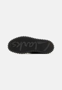 Suela de sneaker de goma negra con patrones de agarre texturizados, que presenta crestas elevadas y un logotipo integrado en el diseño.