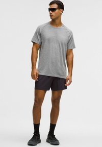 Tricou sport gri cu mânecă scurtă și model texturat, asortat cu pantaloni scurți negri și încălțăminte închisă la culoare. Accesoriile includ ochelari de soare negri.