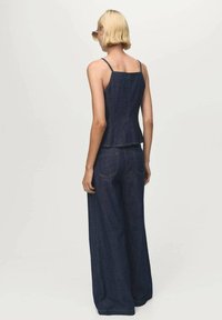Donkerdenim twee-delig outfit met een aansluitend tanktop en wijde broek. Heeft verstelbare banden en zichtbare stikseldetails.