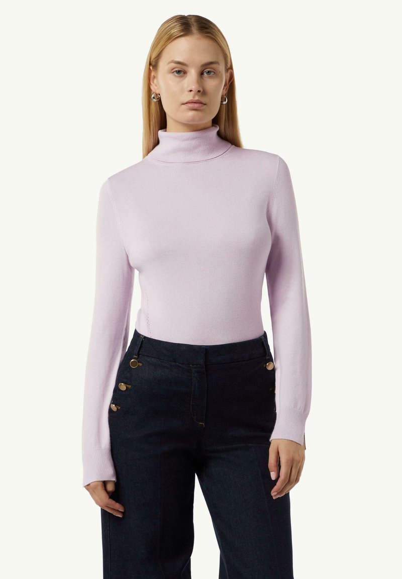 Helllila Rollkragenpullover aus feinem Strickmaterial, kombiniert mit hochtaillierten dunklen Jeans mit goldenen Knopfdetails.