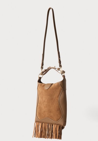 Καφέ σουέτ και δερμάτινη τσάντα με μακριά ρυθμιζόμενη λωρίδα και φούντες στην κάτω άκρη, κρεμασμένη σε απλό φόντο.