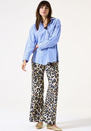 Chemise à rayures bleu clair et blanche avec des manches longues, assortie à un pantalon large à imprimé léopard et des ballerines dorées.