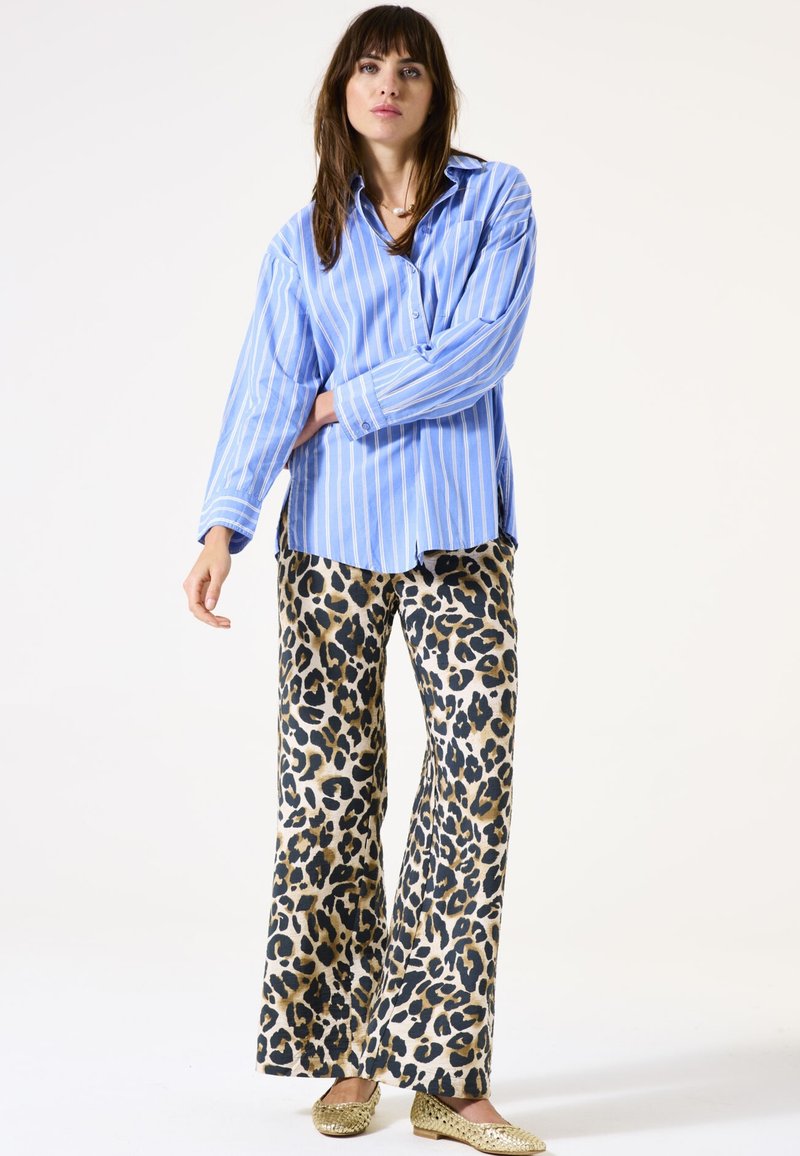 Camisa abotonada de rayas azul claro y blanca con mangas largas, combinada con pantalones de pata de elefante de estampado de leopardo y bailarinas doradas.
