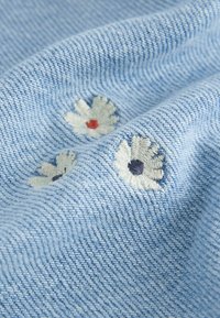 Tissu tissé bleu clair avec trois petites fleurs blanches brodées, chacune avec un centre de couleur différente en rouge, bleu foncé et noir.