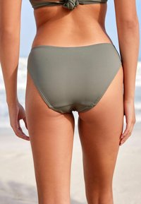 Majtki bikini z wysokim stanem w oliwkowym kolorze, wykonane z gładkiego materiału, z minimalnymi szwami i dopasowanym krojem, idealne na plażę.