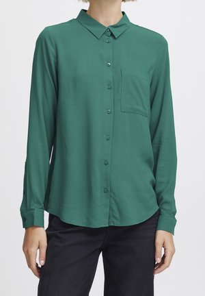 Camicia verde a maniche lunghe con bottoni, realizzata in tessuto morbido, dotata di taschino sul petto e polsini regolabili, con orlo curvo.