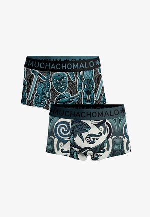 Twee paar boxershorts met donker teal tribale en tiki maskerpattens, met zwarte taillebanden waarop "MUCHACHOMALO" staat.