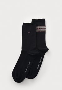 To par svarte sokker ligger flatt, den ene med et flerfarget stripete mønster. Begge har "Tommy Hilfiger"-logoen trykket nederst.