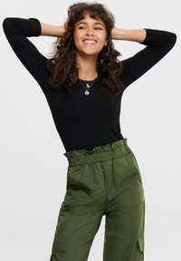 Schwarzes, langärmeliges Oberteil mit taillierter Passform, kombiniert mit lockeren, hoch sitzenden cargo-Hosen in Dunkelgrün mit Seitentaschen.