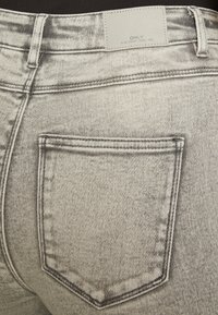 Hallid hallid teksad, millel on kulunud viimistlus, tagaküljel tasku, nähtavad õmblused ja silt, millel on kirjas "ONLY BLUE DENIM ANNO 1995."