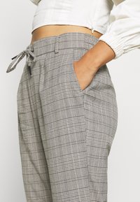 Grijze geblokte broek met een trekkoord in de taille, zijzakken en een relaxte pasvorm. Gemaakt van een gestructureerde stof met een gedetailleerd ruitpatroon.