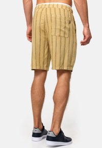 Shorts jaunes à rayures avec une coupe décontractée, dotés d'une taille élastique et d'une poche arrière. Associés à des baskets bleu marine.