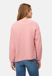 Lichtroze, gestructureerde trui met een losse pasvorm, geribbelde manchetten en zoom. Voorzien van een klein logolabel bij de achterkant van de halslijn. Draagt blauw spijkerbroek.