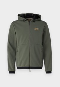 Giacca a vento verde oliva con cappuccio, zip frontale, dettagli neri e una patch con logo. Presenta tasche laterali e una superficie liscia e texture.