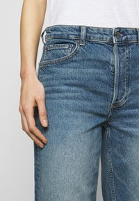 Light blue denim jeans with a straight fit, featuring five pockets, subtle fading, and contrast stitching along the seams.