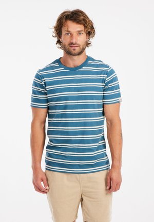 Camiseta de rayas en color azul verdoso y blanco, hecha de algodón. Presenta un cuello redondo y mangas cortas. Se lleva con pantalones cortos beige.