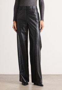 Pantalons larges en cuir noir avec une texture lisse, taille haute et poches avant discrètes, associés à un haut ajusté à côtes.